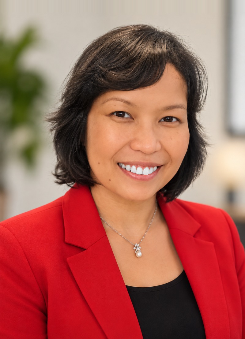 Terri Abellera, smiling, in a red blazer and pendant necklace